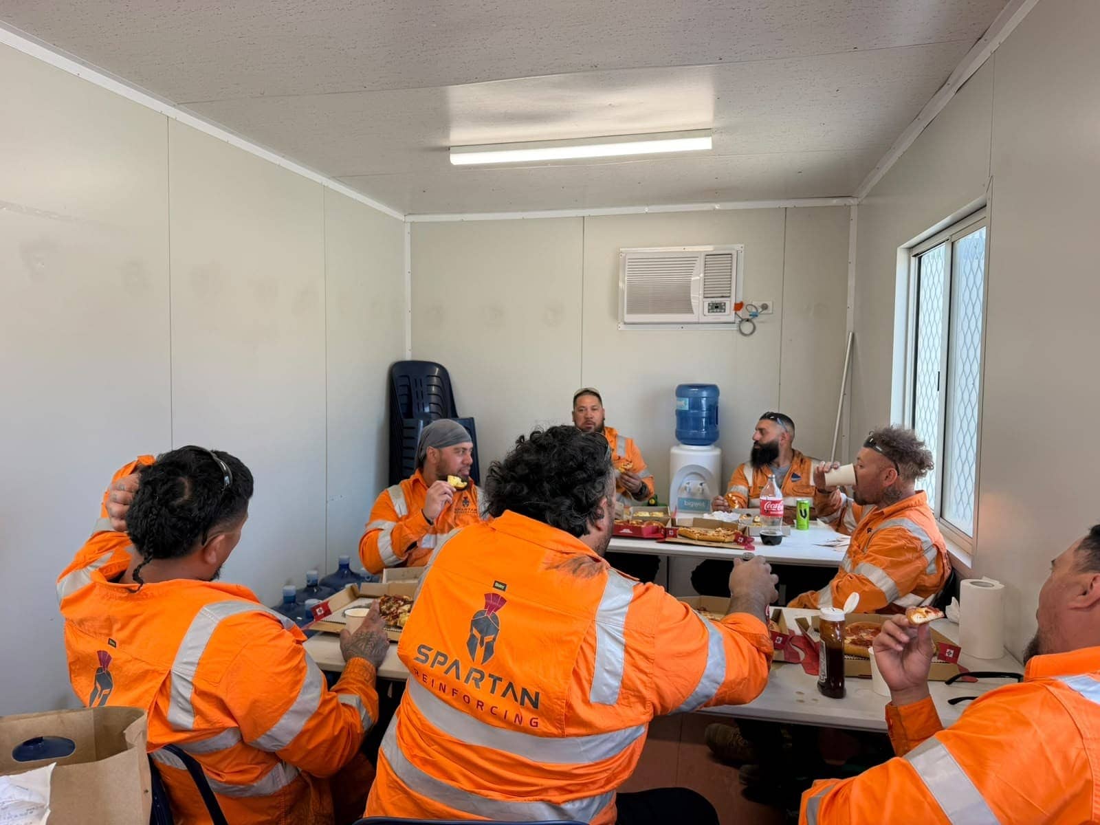 The Spartan crew in Spartan Reinforcing hi-vis, sharing lunch in the site shed